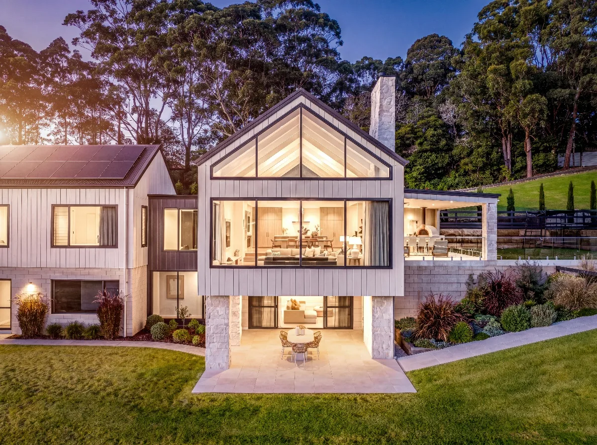 Modern home with illuminated windows and landscaped gardens at dusk